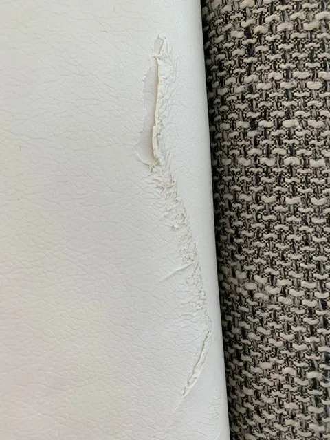 Aufgerissene Stelle im Leder, die den Blick auf das Trägergewebe freigibt | Ecksofa mit Ledersockel Neubezug Aus der Polsterwerkstatt Egora: Aufgerissene Stelle im Leder, die den Blick auf das Trägergewebe freigibt (Ecksofa mit Ledersockel, Sofa neu beziehen)